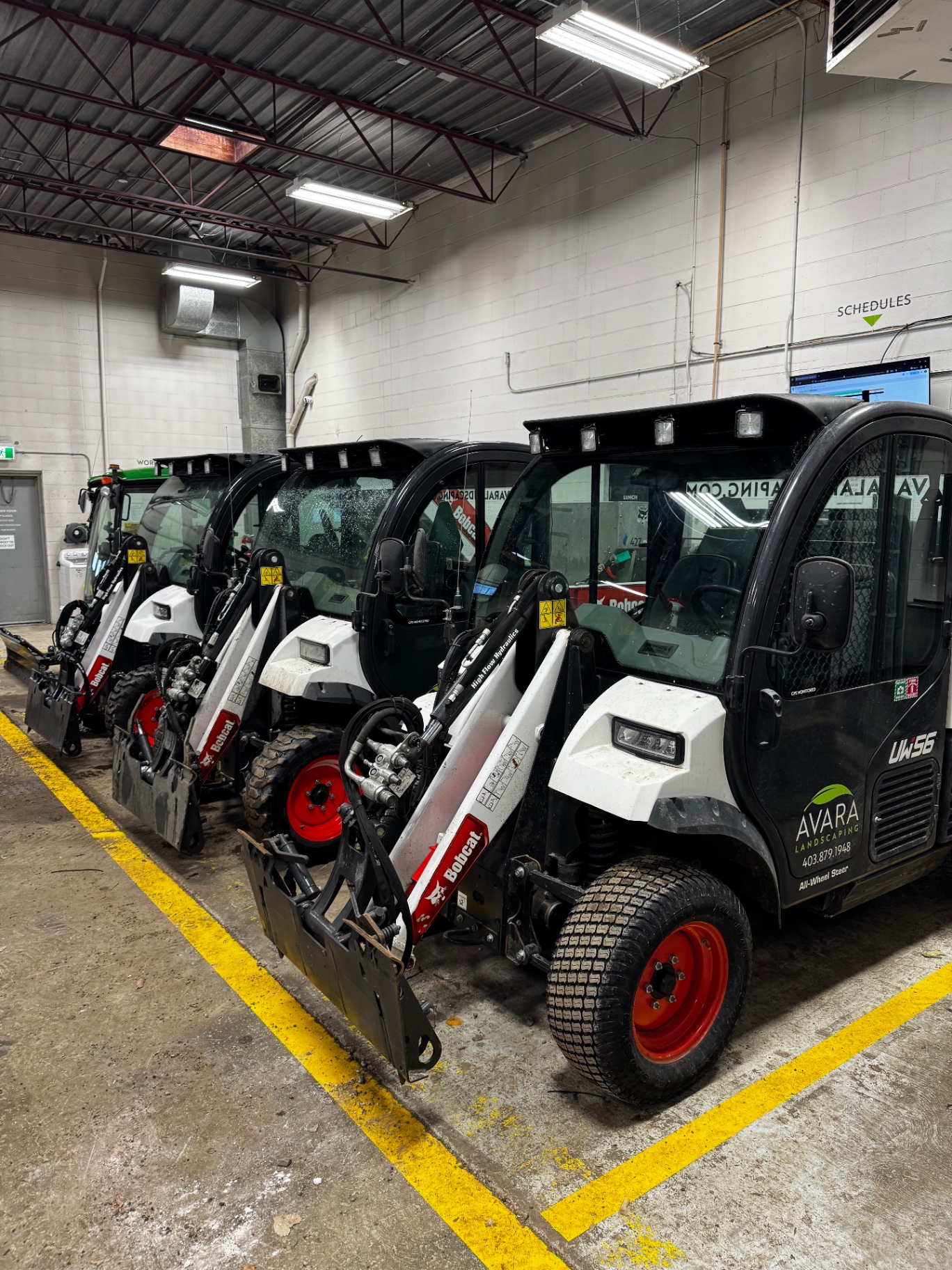 Avara Landscaping snow fleet staged inside heated indoor facility — Bobcat Toolcats and skid steers ready for dispatch