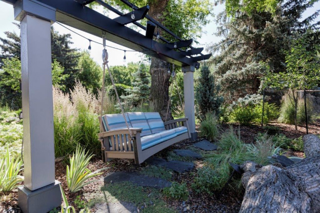Garden swing under a dark steel pergola with bistro lighting